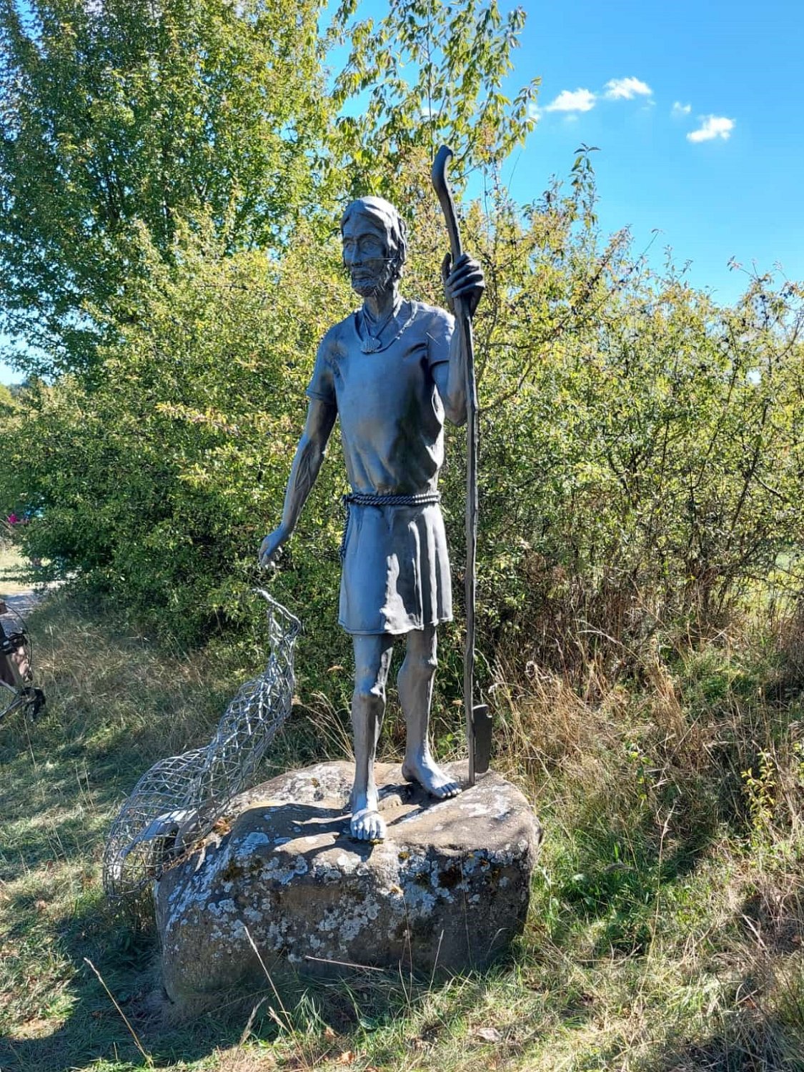 260915gnadenweiler (09e).jpg - Die Statue mit dem Netz direkt neben der Wallfahrtskapelle „Maria, Mutter Europas“ stellt den Apostel Jakobus den Älteren dar. Die von dem Breisacher Künstler Helmut Lutz gestaltete Pilgerskulptur am Beuroner Jakobsweg zeigt Jakobus im Moment seiner Berufung durch Jesus. Das Netz symbolisiert dabei seinen ursprünglichen Beruf als Fischer, den er hinter sich lässt, um als Jünger Jesu zu einem „Menschenfischer“ und Verkünder der frohen Botschaft zu werden.